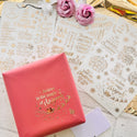 A small red paper wrapped gift box is sitting on 3 sheets of Get Inspired's Christmas Greetings Gold Foil small transfes.