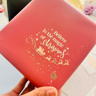 A red paper wrapped present box features Get Inspired's Christmas Greetings Gold Foil small transfer that reads: Believe in the magic of Christmas.