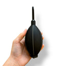 A hand is shown holding a black large air puffer against a white background.