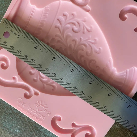 Pink decorative silicone mold with intricate patterns and a ruler for scale on a wooden surface.