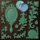 An open container of Dadarkar Art's Emerald Patina Metallic Wax Mousse is amongst resin silicone mold castings of a vintage hand mirror and various corner and accent rose flourishes.