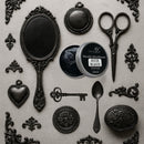 An open container of Dadarkar Art's Rich Black Metallic Wax Mousse is amongst resin silicone mold castings of vintage items including a hand mirror, scissors, a spoon, a key, and various corner and accent flourishes.