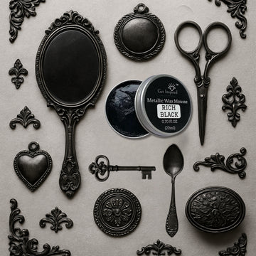 An open container of Dadarkar Art's Rich Black Metallic Wax Mousse is amongst resin silicone mold castings of vintage items including a hand mirror, scissors, a spoon, a key, and various corner and accent flourishes.