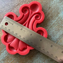 Red silicone mold with decorative pattern on a wooden surface, measured by a ruler.