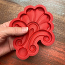 Red silicone mold with decorative design held by a hand on a wooden surface