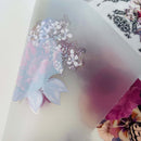 A close-up of a backside of a small rub-on transfer on a clear acetate sheet.