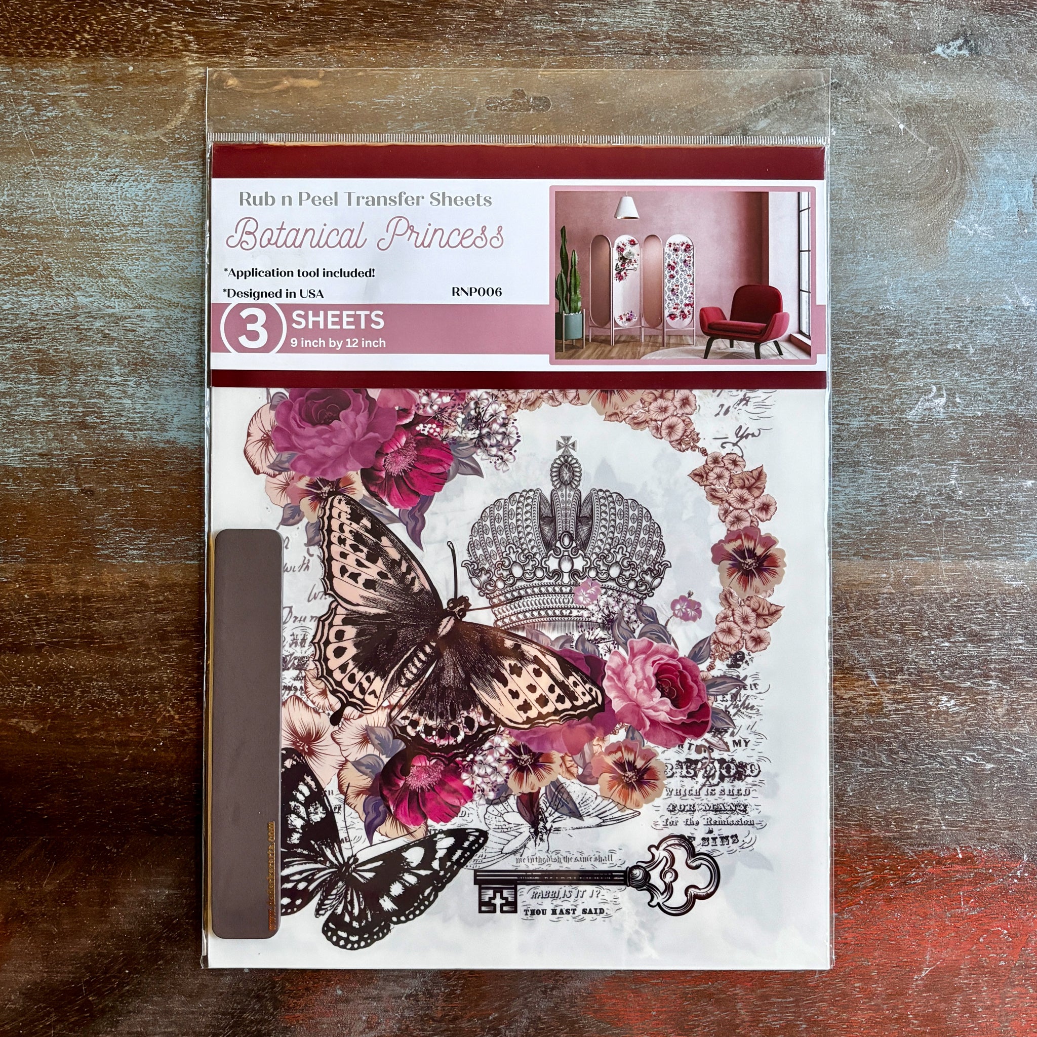 A package of Dadarkar Art’s Get Inspired Botanical Princess rub-on transfers is against a dark wood background.