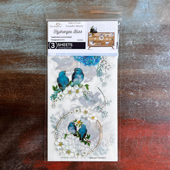 A package of Dadarkar Art’s Get Inspired Hydrangea Bliss rub-on transfers is against a dark wood background.