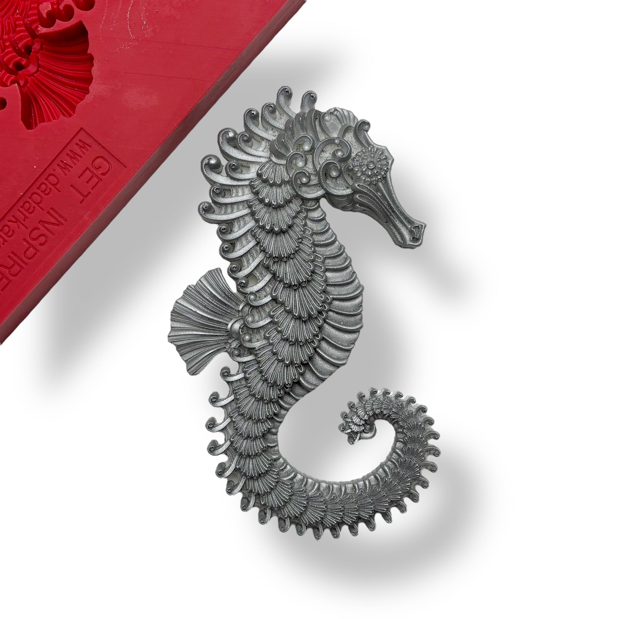 A red silicone mold and silver colored silicone mold casting of a seahorse is shown against a white background. 