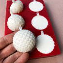A red silicone mold and white resin castings of 6 half ornament bulbs are against a beige background. A hand is shown holding one of the castings.