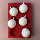 A red silicone mold and white resin castings of 6 half ornament bulbs are against a beige background. Two of the castings are shown placed together to create a full ornament.