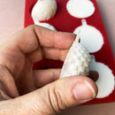 A red silicone mold and white resin castings of 6 half ornament bulbs are against a beige background. A hand is shown holding one of the castings.
