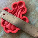 Red silicone mold with decorative pattern on a wooden surface, measured by a ruler.