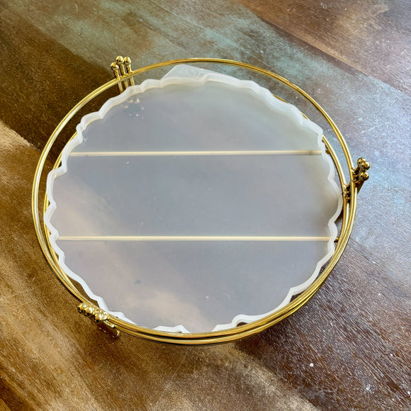 A silicone mold to make a 10.62" resin tray and a gold stand are against a wood background.