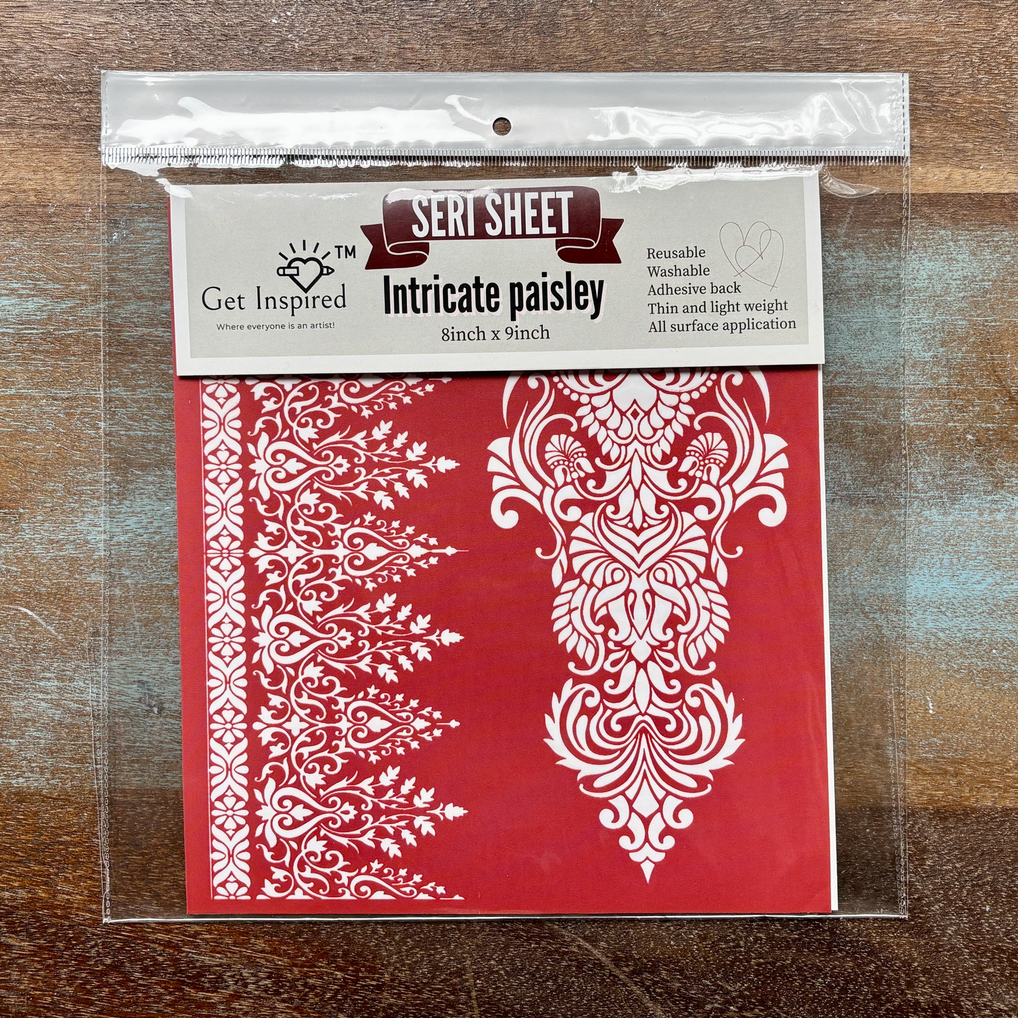 A package of Dadarkar Arts by Get Inspired's Intricate Paisley Silkscreen Stencil is against a wood background.