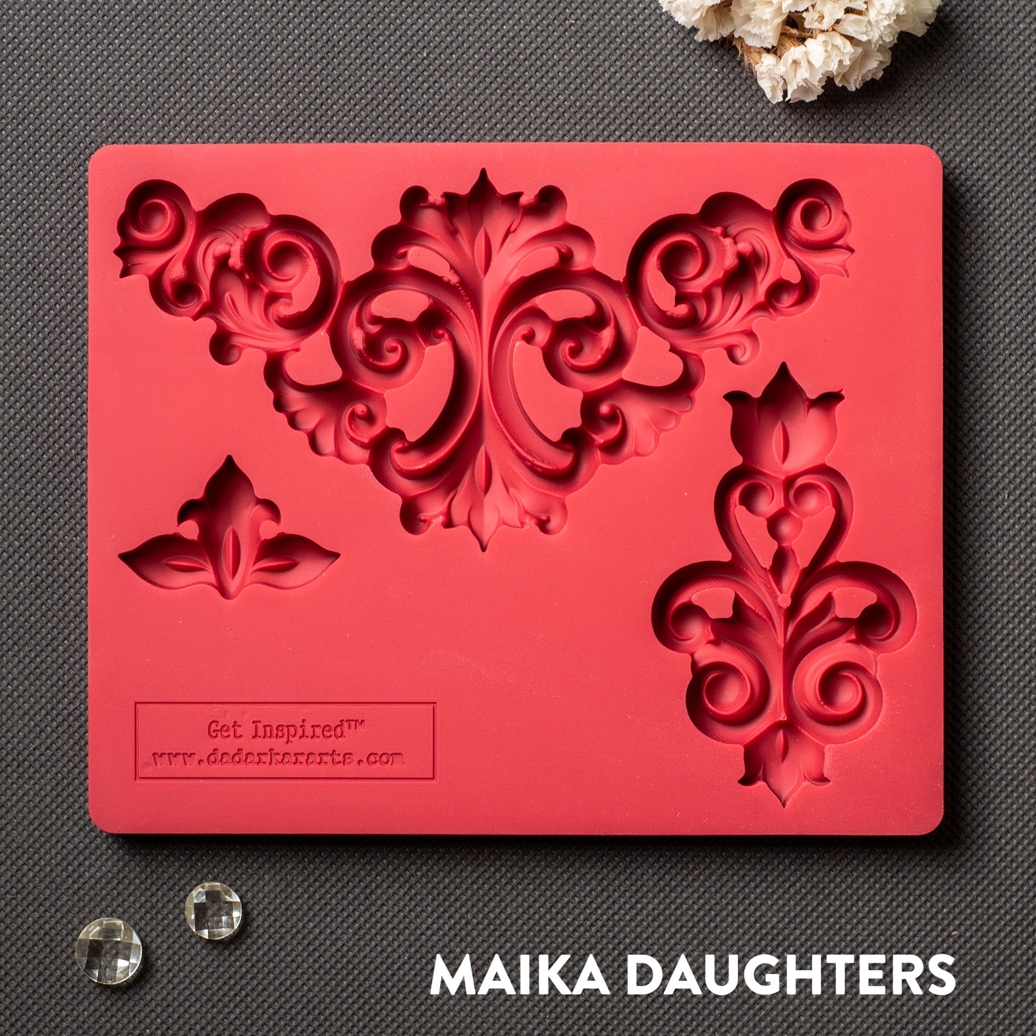 A red silicone mold that features 3 avant-garde style flourish corner pieces is against a dark grey material background.