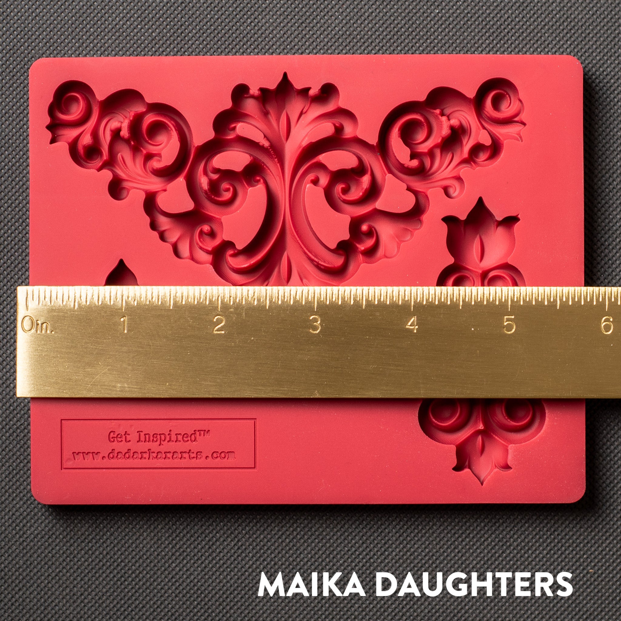 A red silicone mold that features 3 avant-garde style flourish corner pieces is against a dark grey material background. A gold ruler reading 5.75" length sits on the mold.