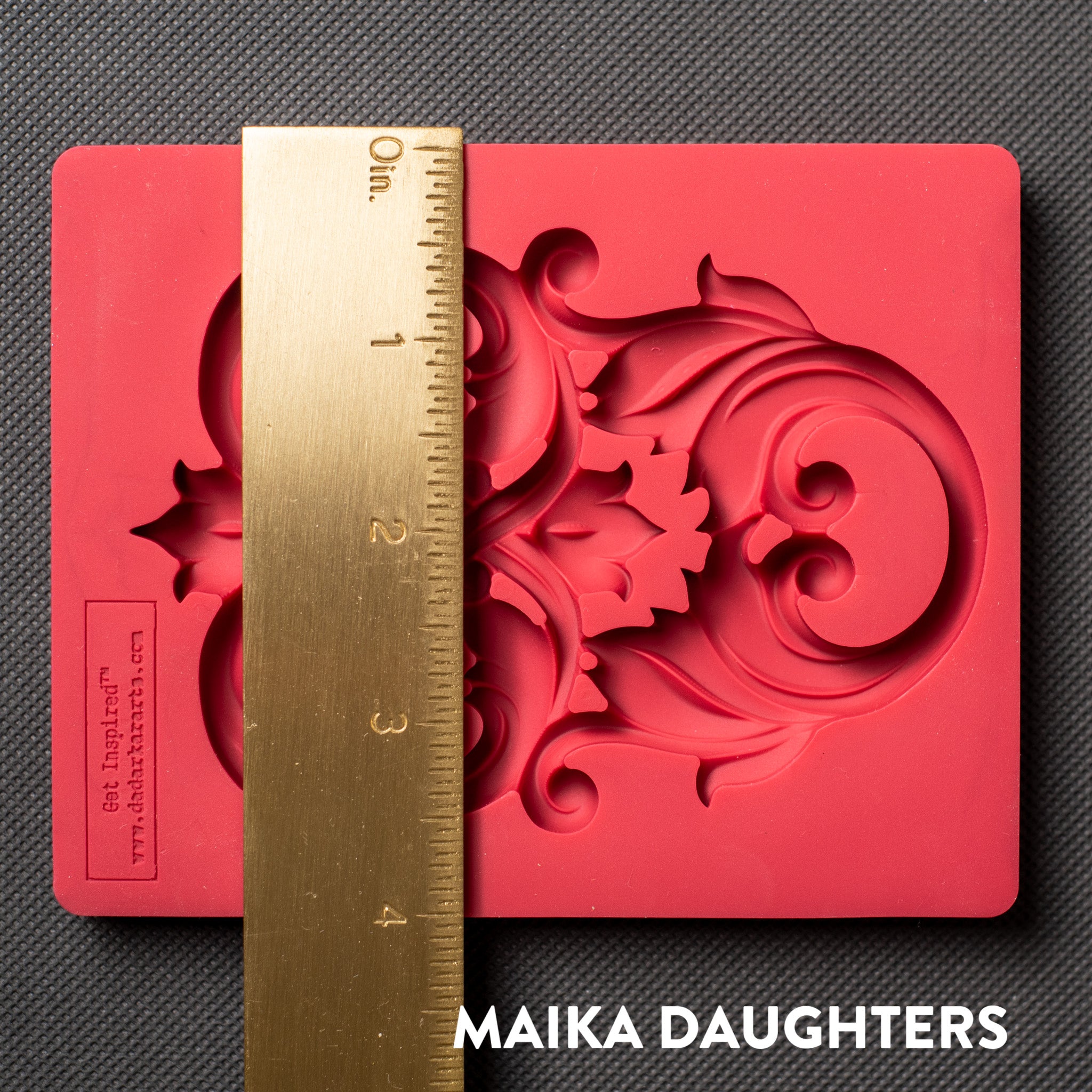 A red silicone mold that features an intricate flourish accent piece is against a dark grey material background. A gold ruler reading 4" height sits on the mold.