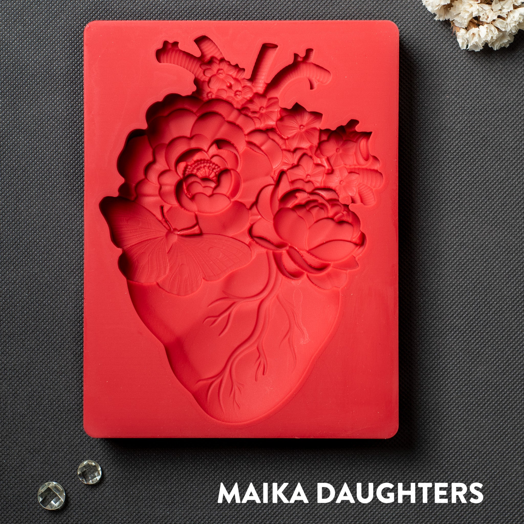 A red silicone mold of an anatomical heart with flowers coming out of it is against a dark grey background.