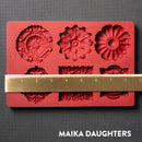 A red silicone mold featuring 6 ornate medallions is against a dark grey background. A gold ruler reading 8.5 inches width sits on the mold.