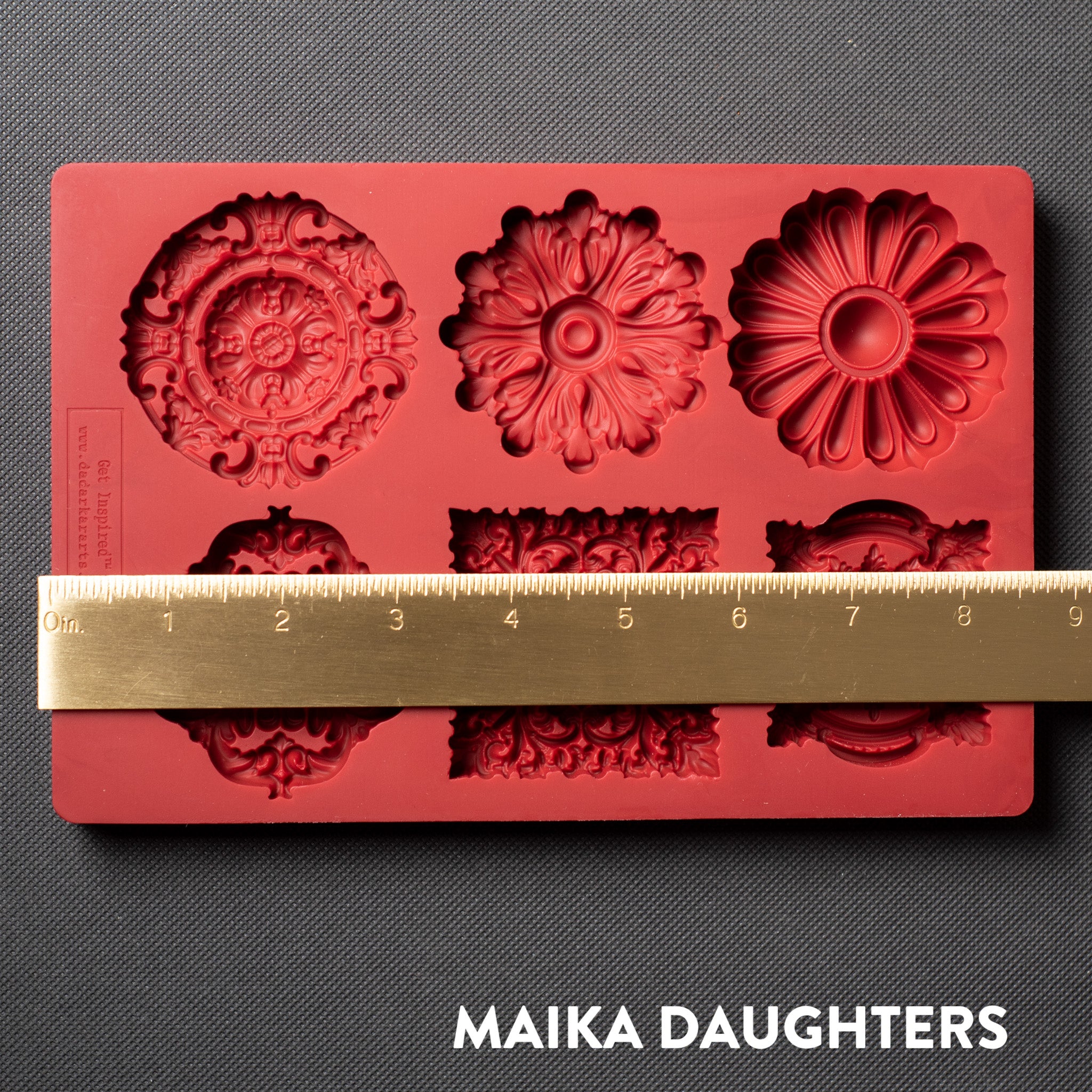 A red silicone mold featuring 6 ornate medallions is against a dark grey background. A gold ruler reading 8.5 inches width sits on the mold.