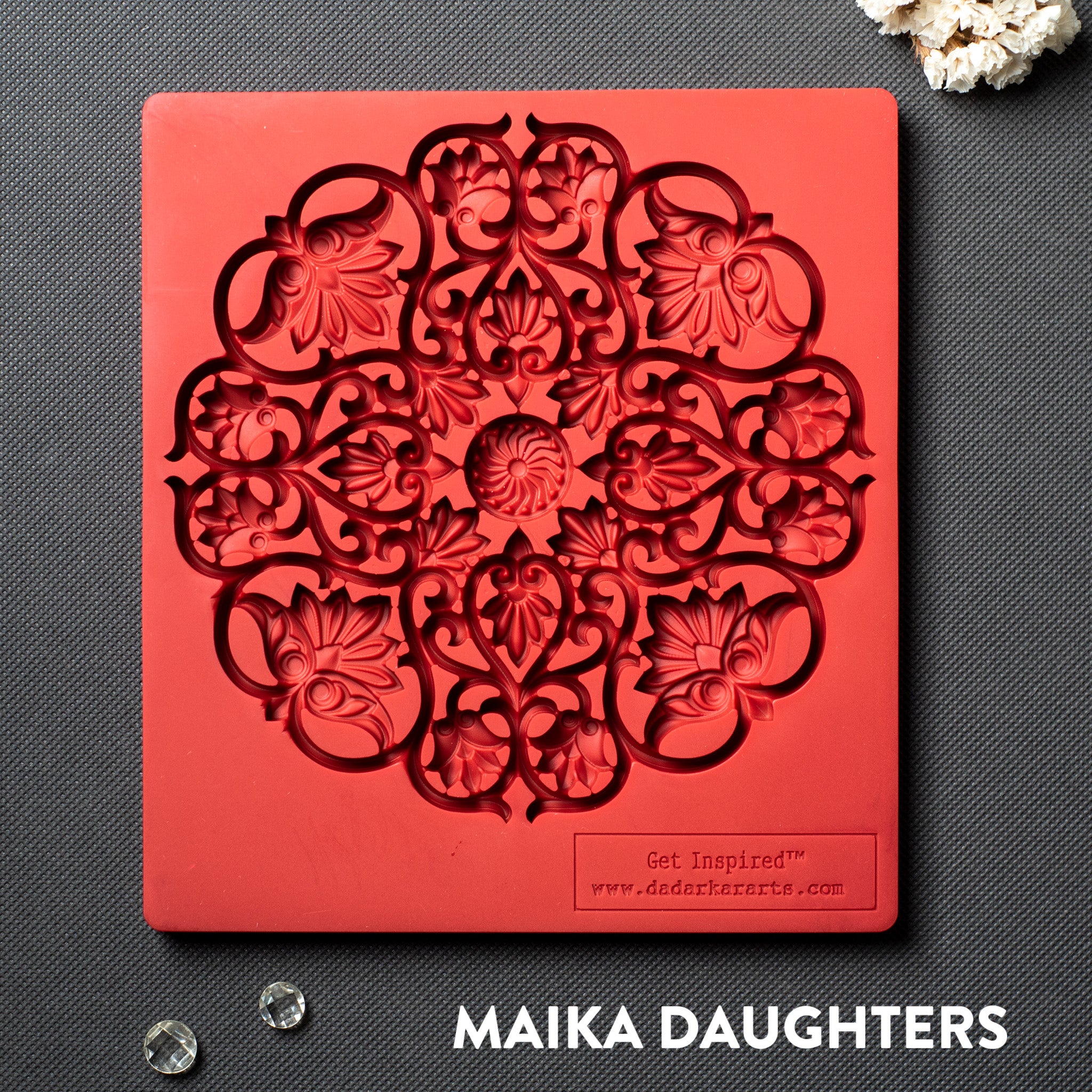 A red silicone mold of a large mandala with lotus flowers in it is against a dark grey background.