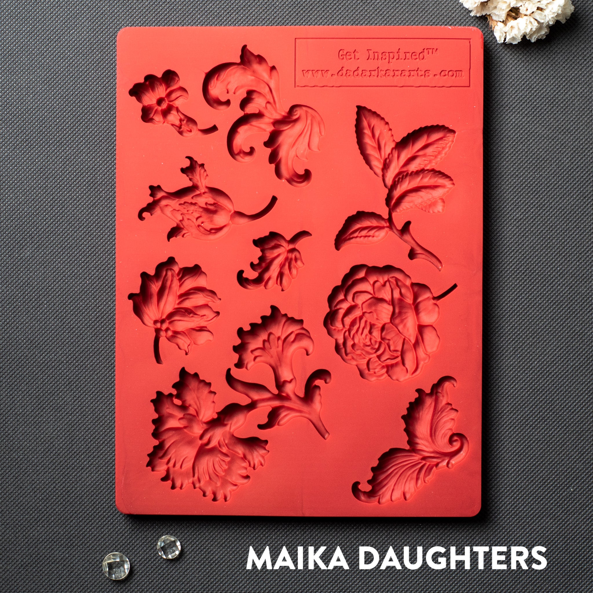 A red silicone mold featuring single flower blooms and loose leaves is against a dark grey material background.