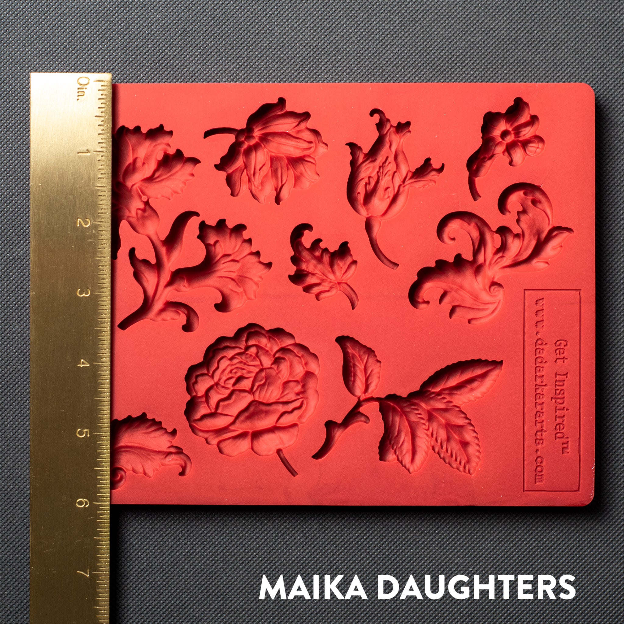 A red silicone mold featuring single flower blooms and loose leaves is against a dark grey material background. A gold ruler reading 6" height sits on the mold.