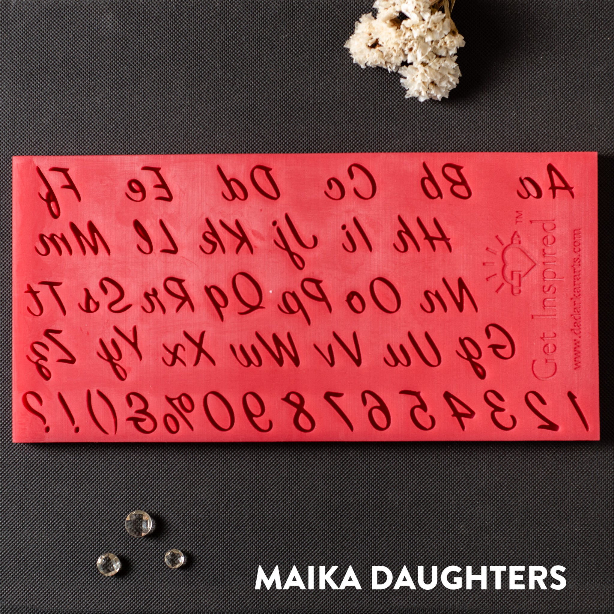 A red silicone mold of the English alphabet in script writing, numbers 0-9, and punctuations is against a dark grey background.