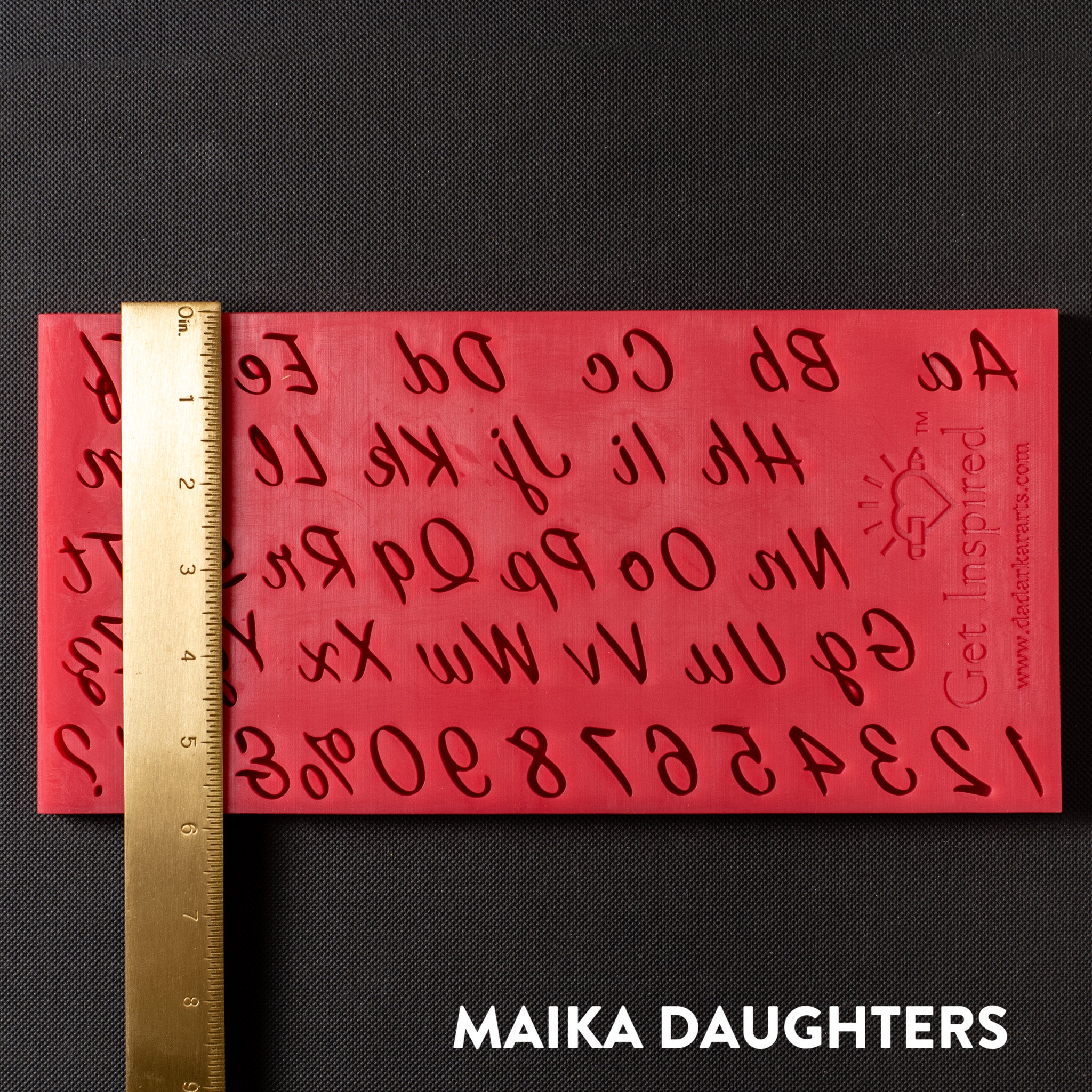 A red silicone mold of the English alphabet in script writing, numbers 0-9, and punctuations is against a dark grey background. A gold ruler reading 6" height sits on the mold.