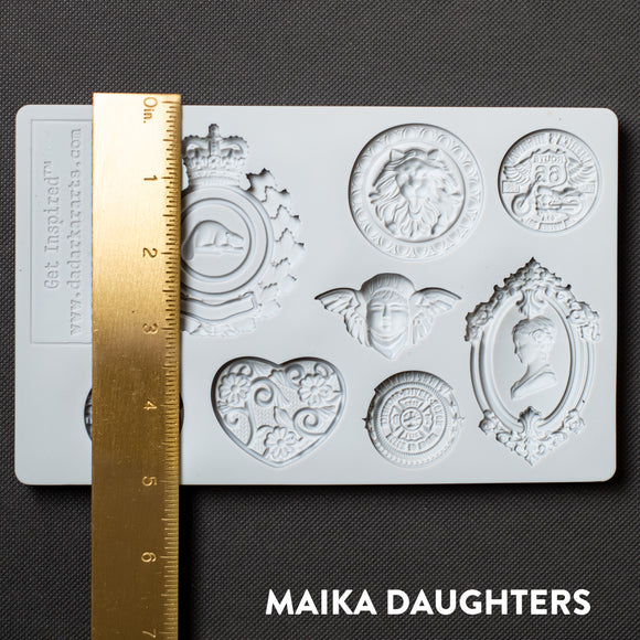 A light grey silicone mold of 8 ornate regal medallions is against a dark grey background. A gold ruler reading 5 inches height sits on the mold.