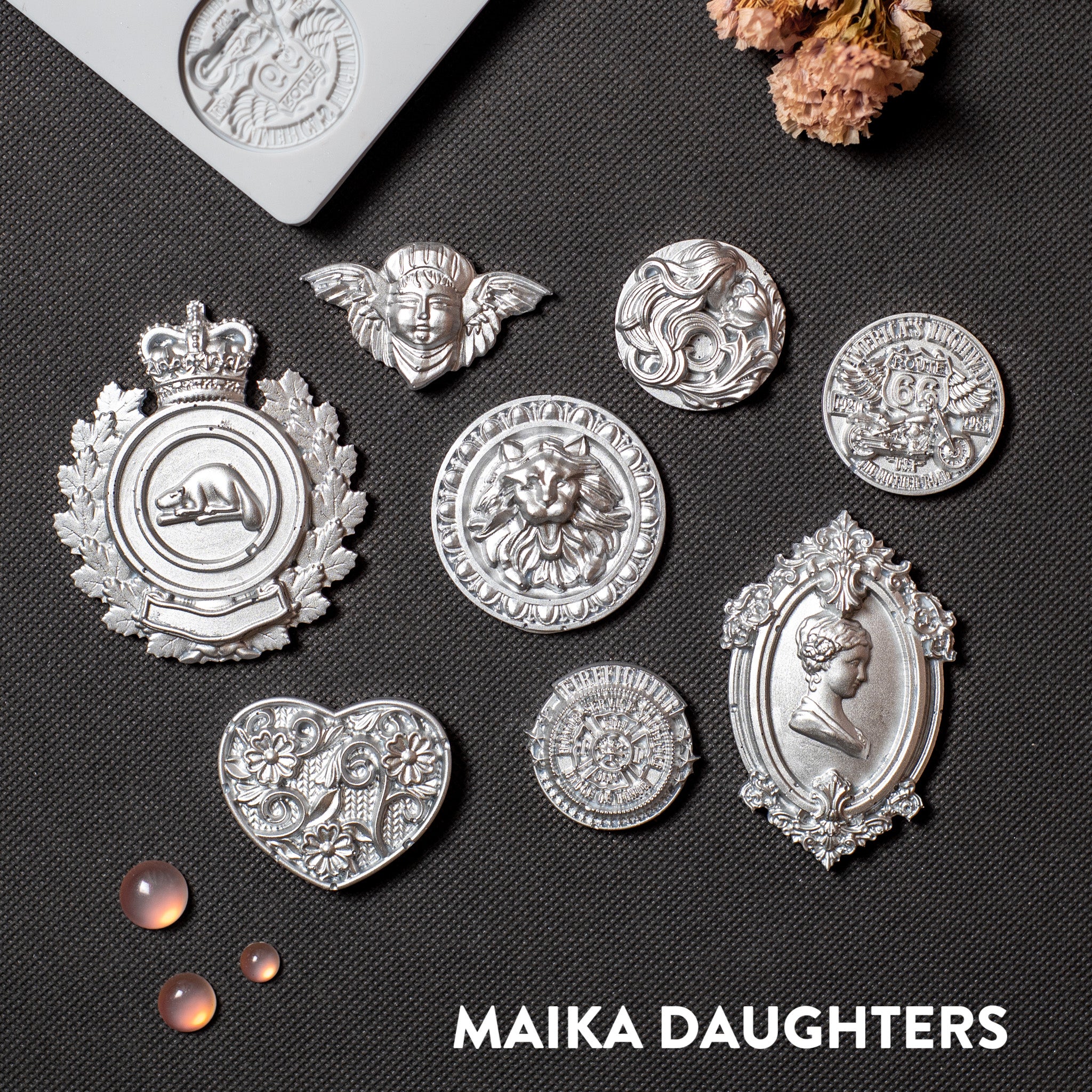 Silver colored silicone mold castings of 8 ornate regal medallions are against a dark grey background.