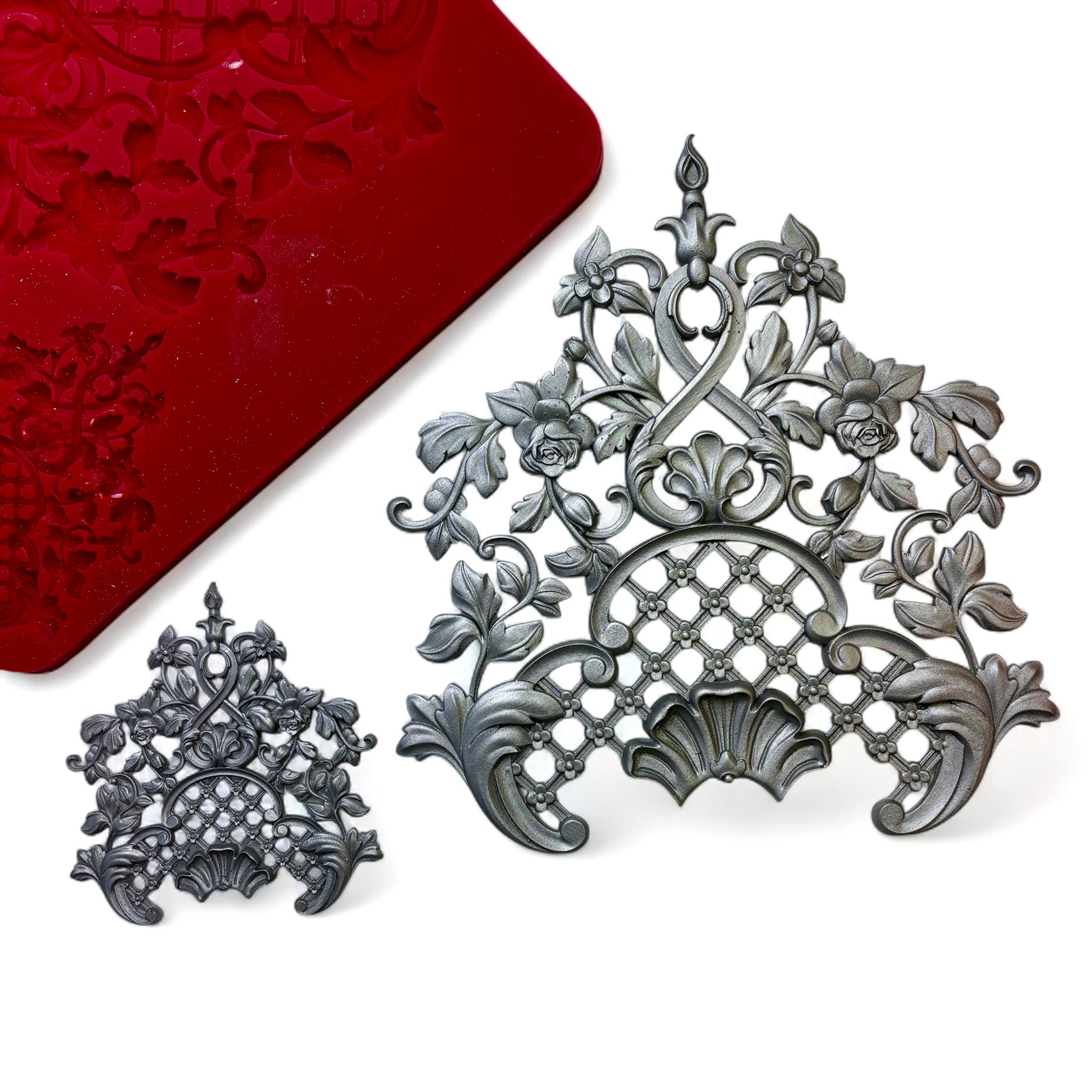 A red silicone mold and silver colored castings of 1 large and 1 small vintage floral lattice center piece design are against a white background.