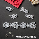 Silver colored silicone mold castings that features 4 small corner flourishes and one larger border are against a dark grey material background.