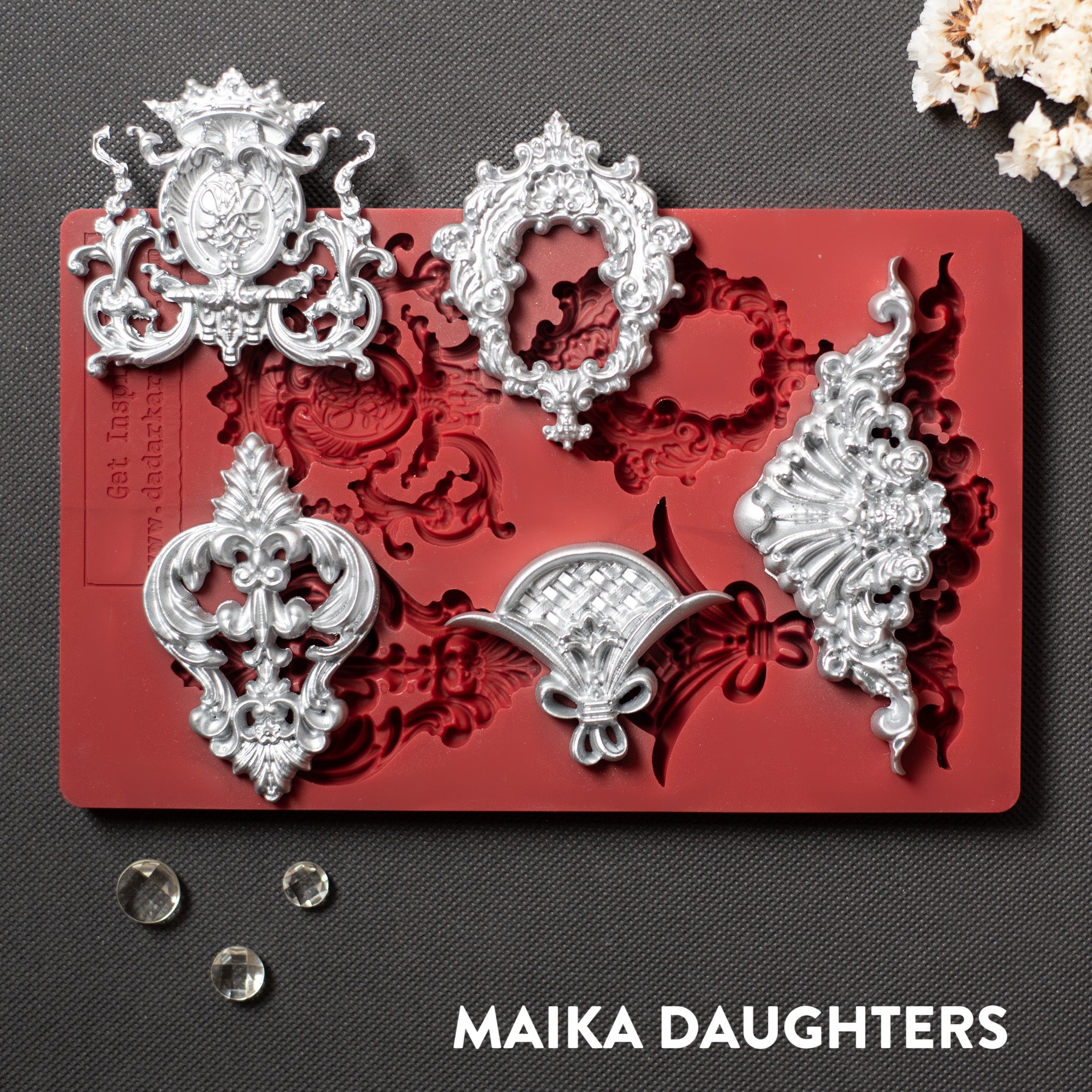 A red silicone mold and silver colored castings of 5 regal center accent pieces are against a dark grey material background.