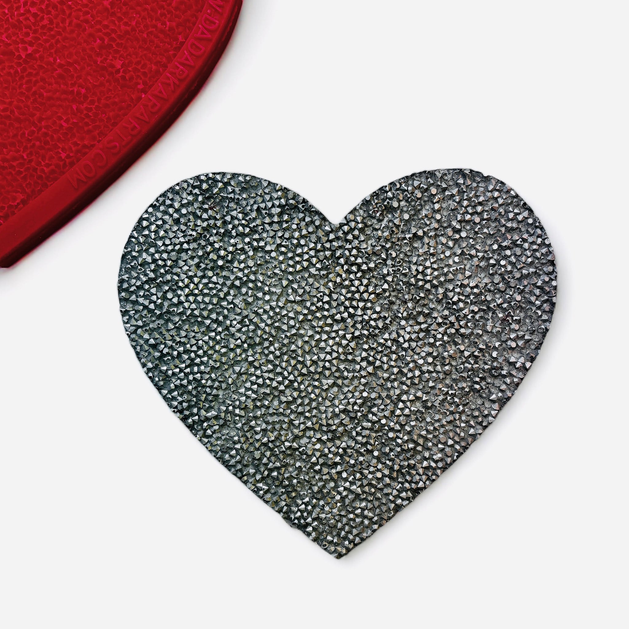 A silver colored casting of a large textured heart is against a white background. 