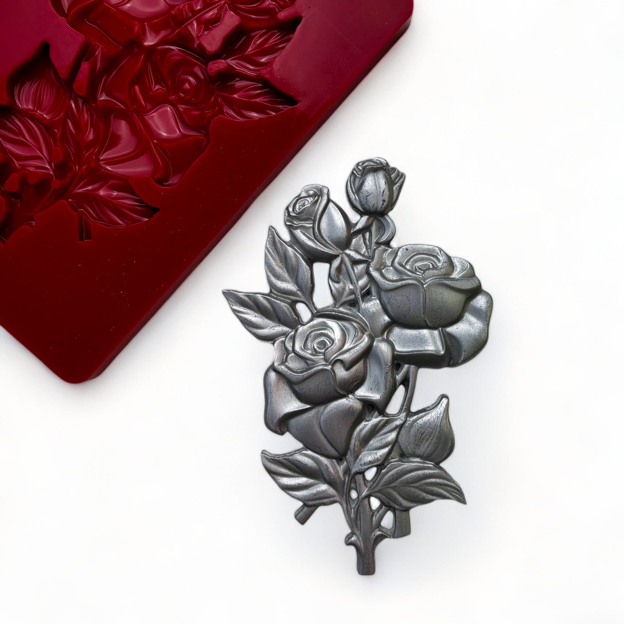 A red silicone mold and silver colored casting of a small bouquet of roses are against a white background.