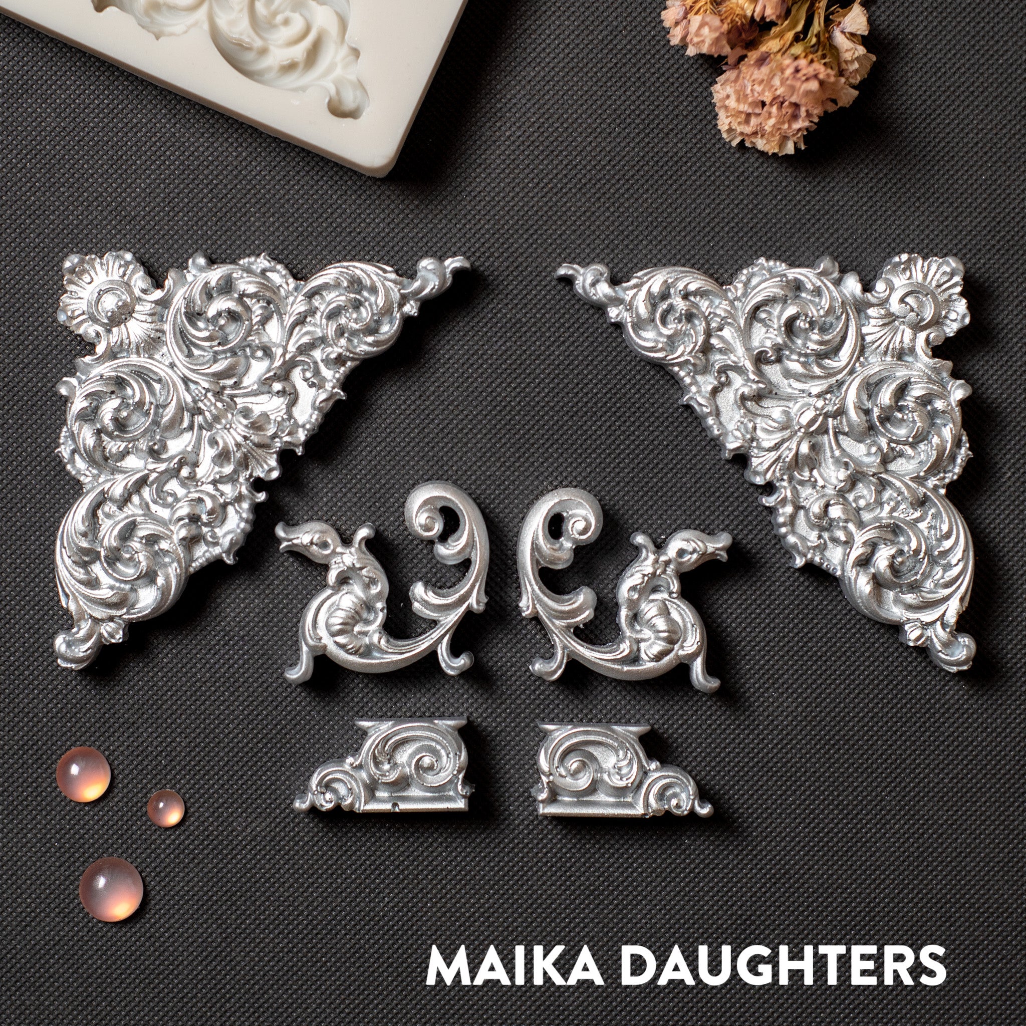 Silver colored castings of ornate corner and accent pieces are against a dark grey background.