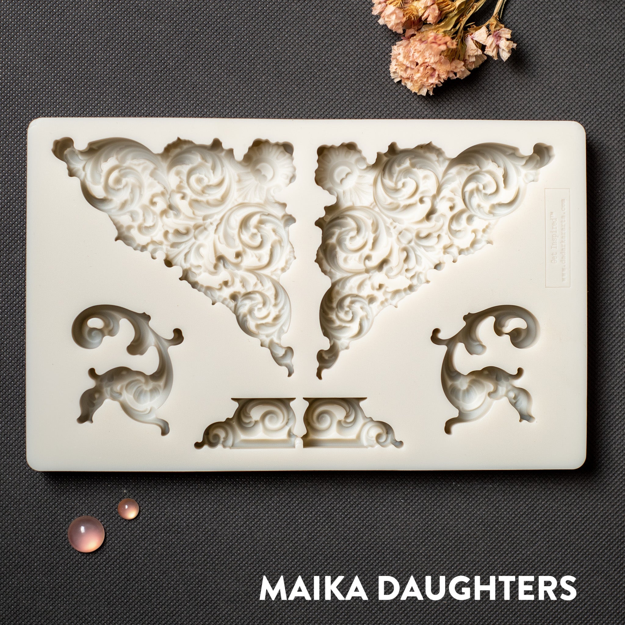 A light beige silicone mold of ornate corner and accent pieces is against a dark grey background.