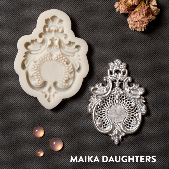 A light beige silicone mold and silver colored casting of a large chandelier style crown medallion are against a dark grey background.