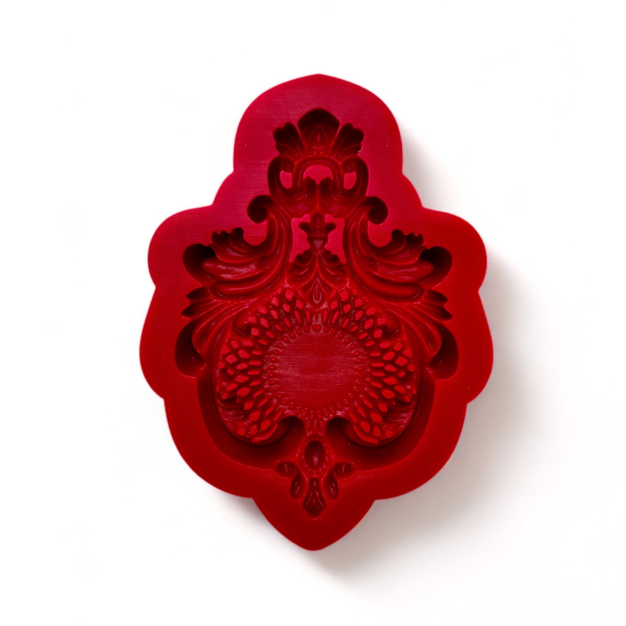 A red silicone mold of a large chandelier style crown medallion is against a dark grey background.