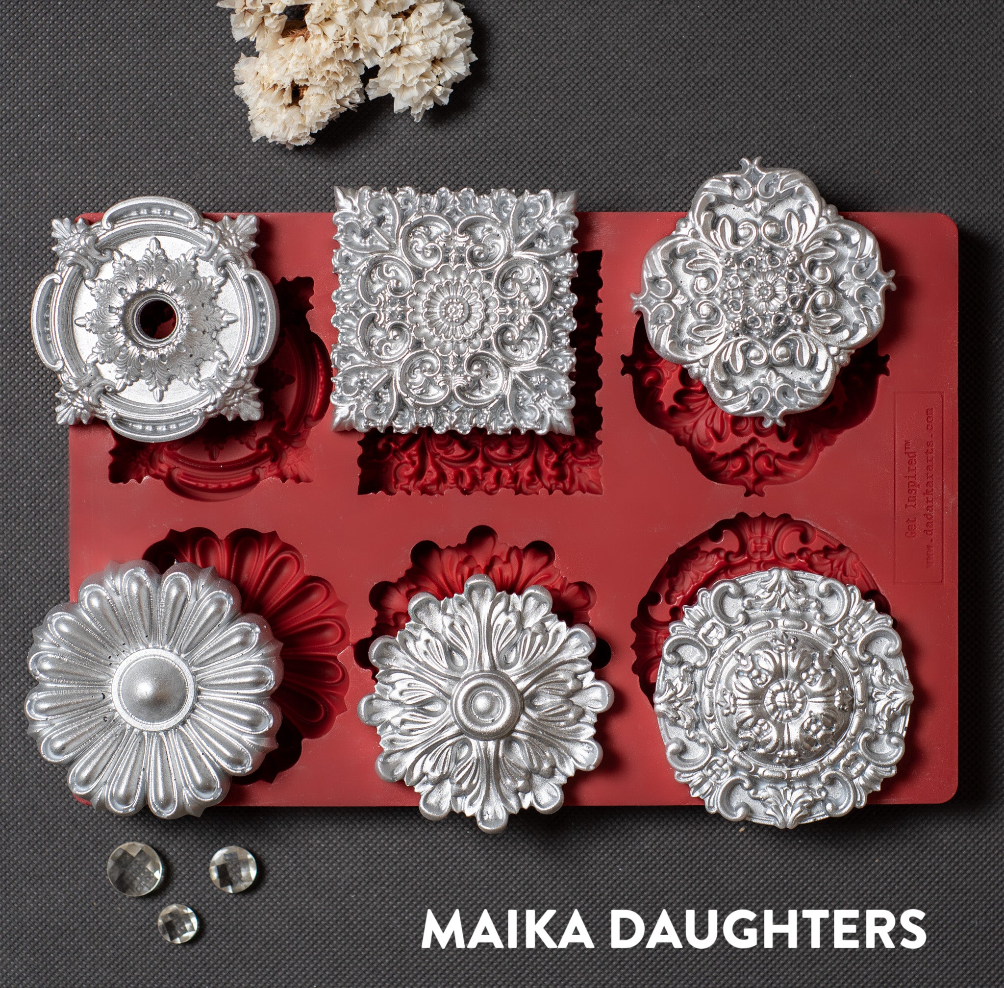 A red silicone mold and silver colored castings of 5 round and 1 square ornate medallions are against a dark grey background.