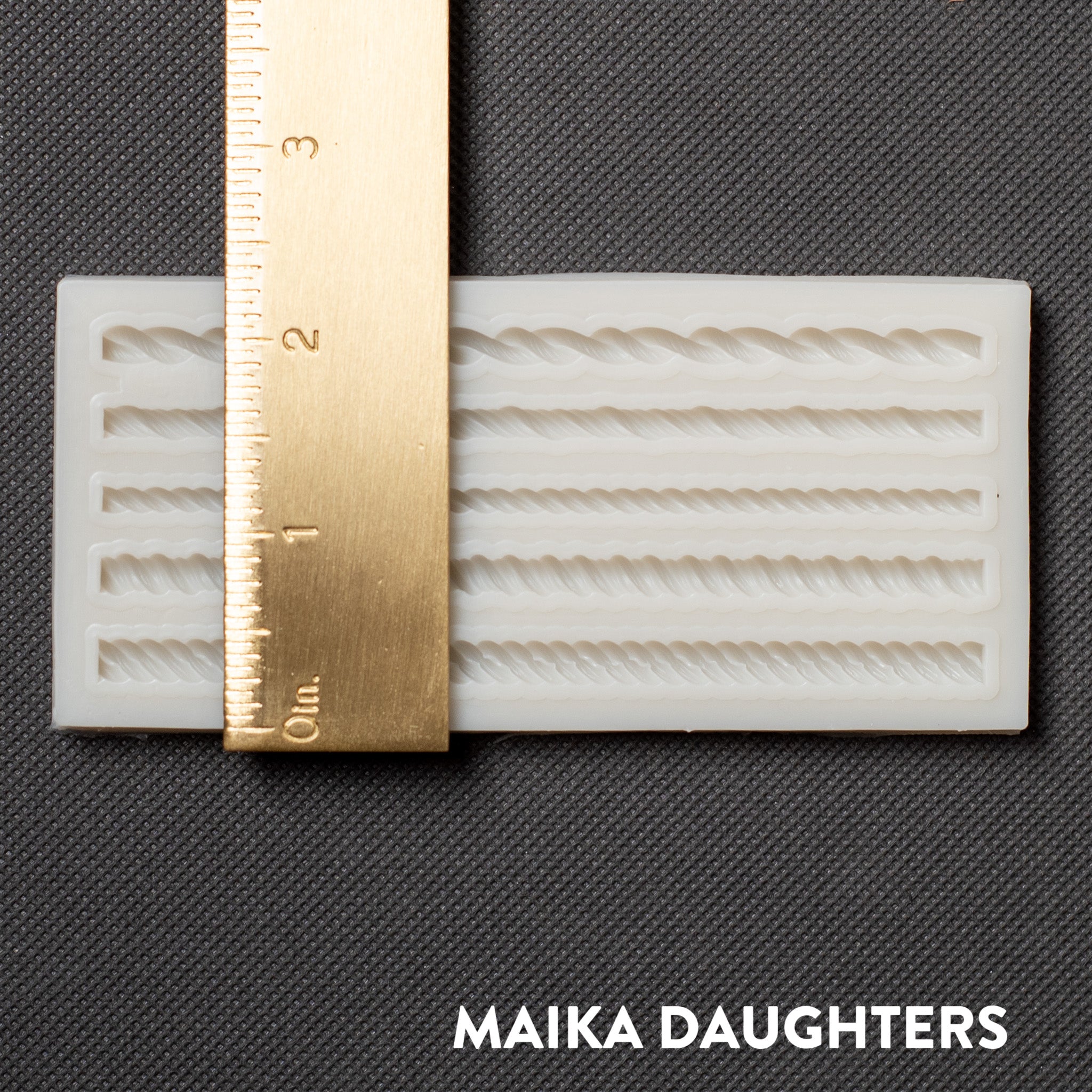 A light beige silicone mold of Get Inspired by Dadarkar Arts Mini Ropes are against a dark grey background. A gold ruler reading 2.5 inches height sits on the mold.