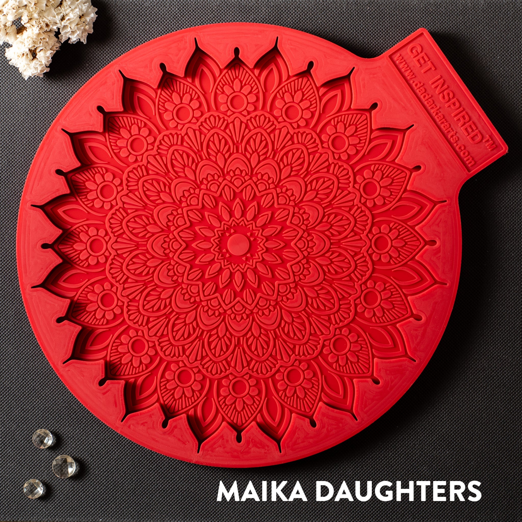 A red silicone mold of a large mandala with paisleys is against a dark grey background.