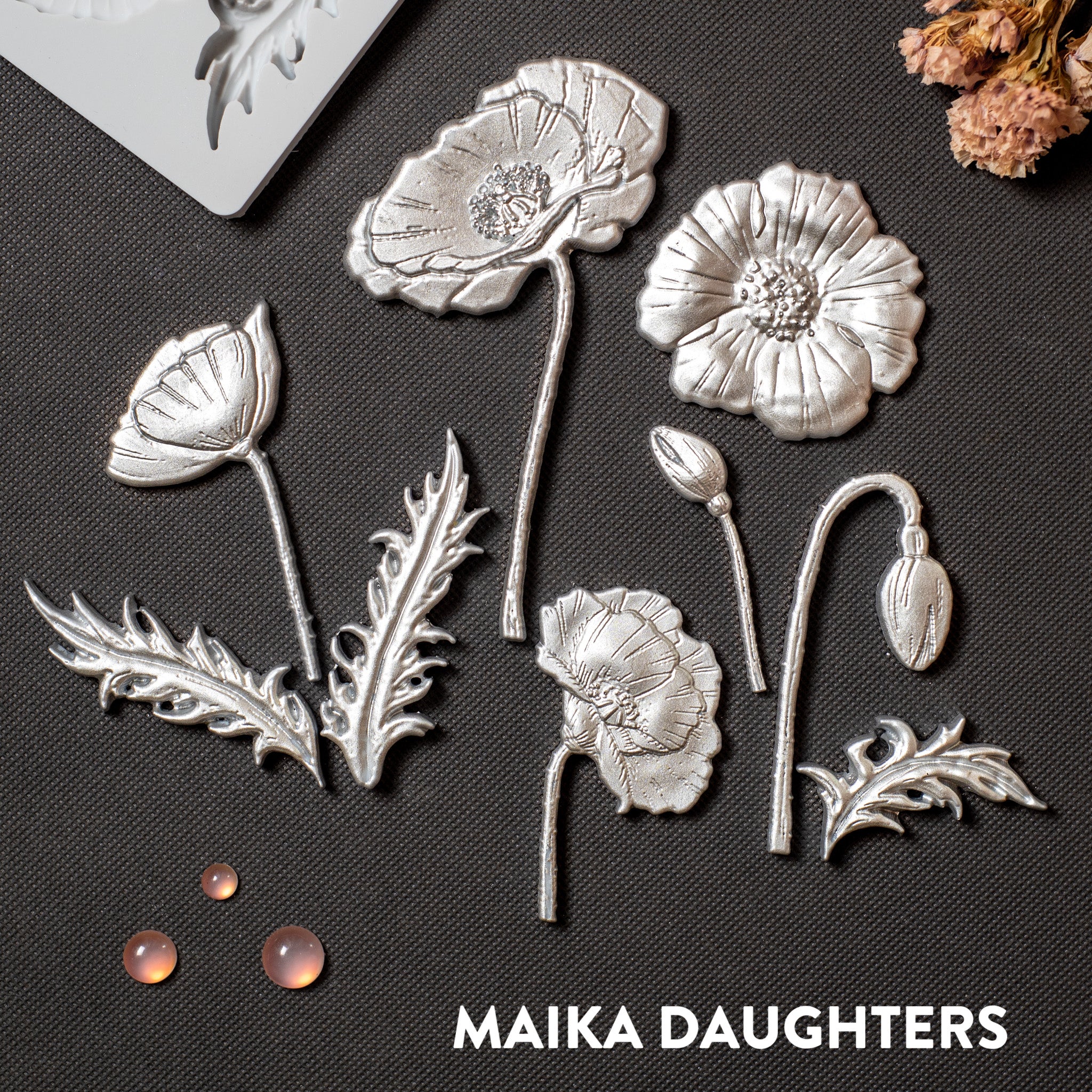 Silver colored silicone mold castings of flower blooms, buds, and leaves are against a dark grey background.