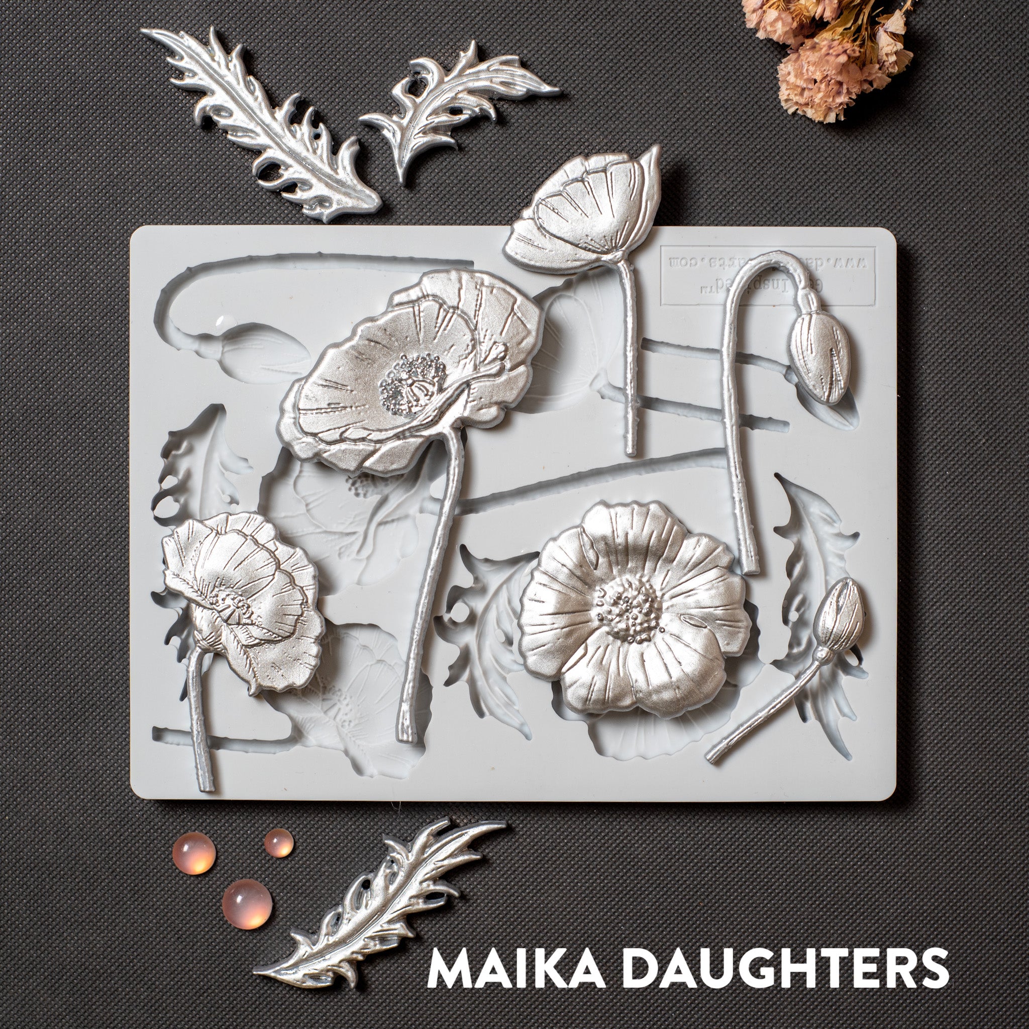 A light grey silicone mold and silver colored castings of flower blooms, buds, and leaves are against a dark grey background.