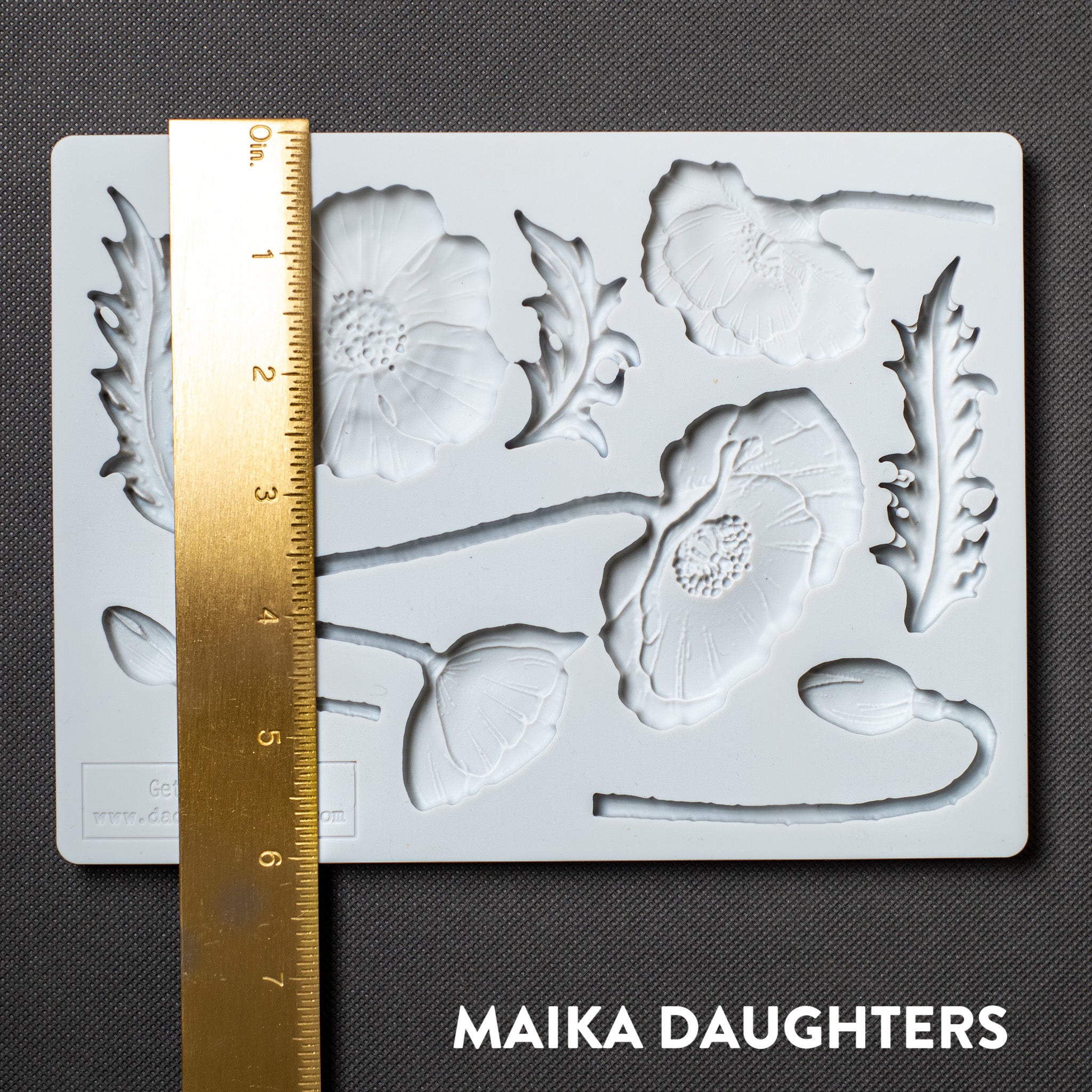 A light grey silicone mold featuring flower blooms, buds, and leaves is against a dark grey background. A gold ruler reading 6 inches height sits on the mold. 