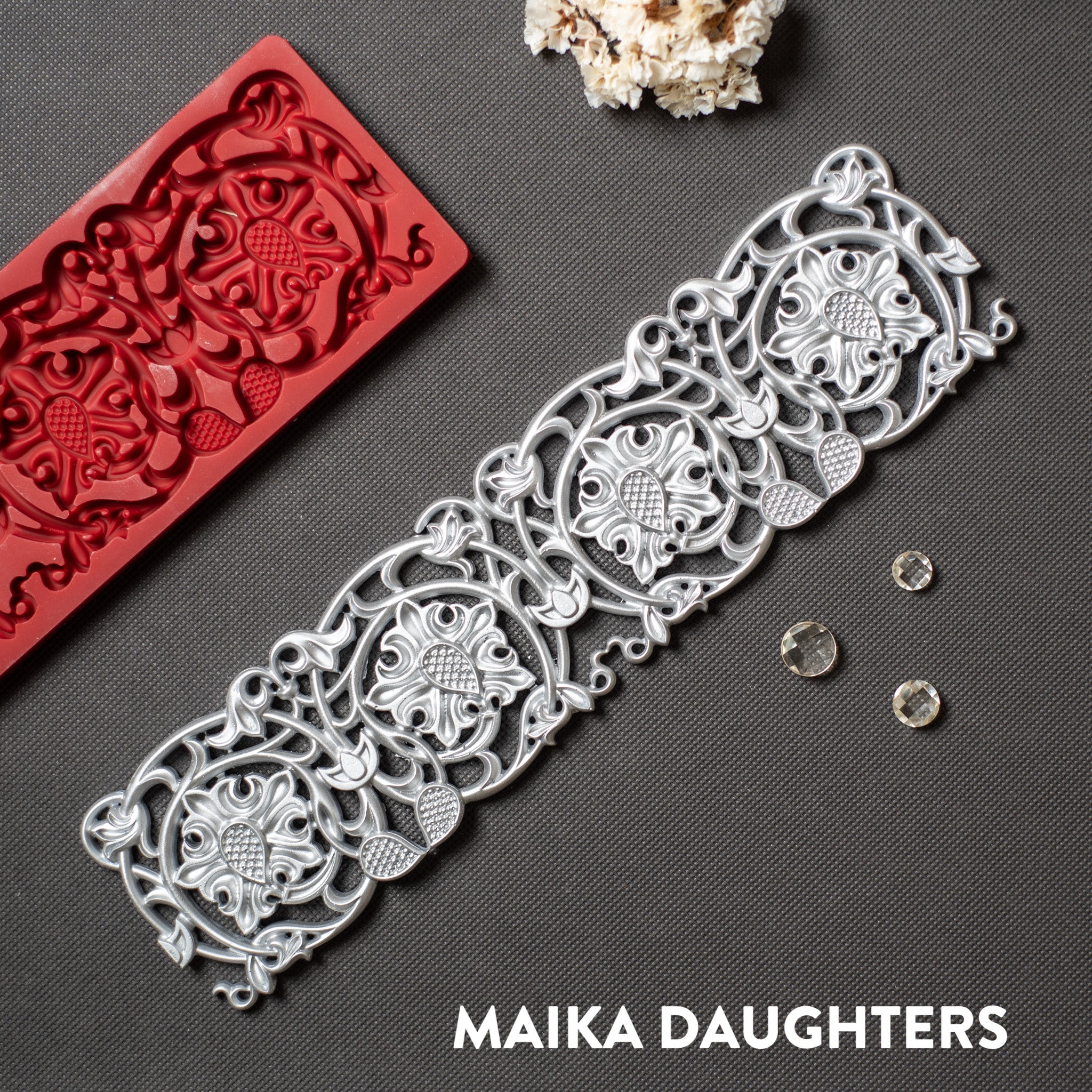 A red silicone mold and silver colored casting of an ornate border is against a dark grey background.