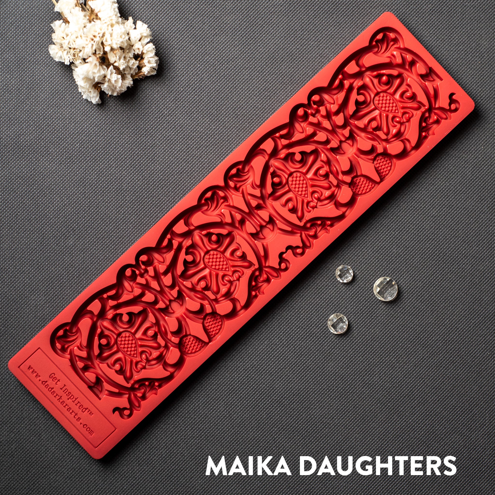 A red silicone mold of an ornate border is against a dark grey background.