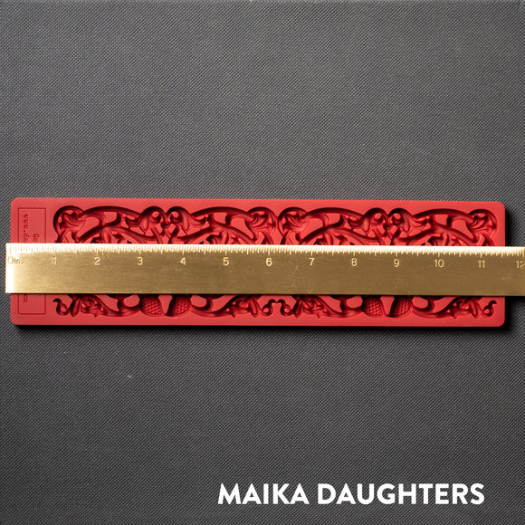 A red silicone mold of an ornate border is against a dark grey background. A gold ruler reding 11.5 inches length sits on the mold.